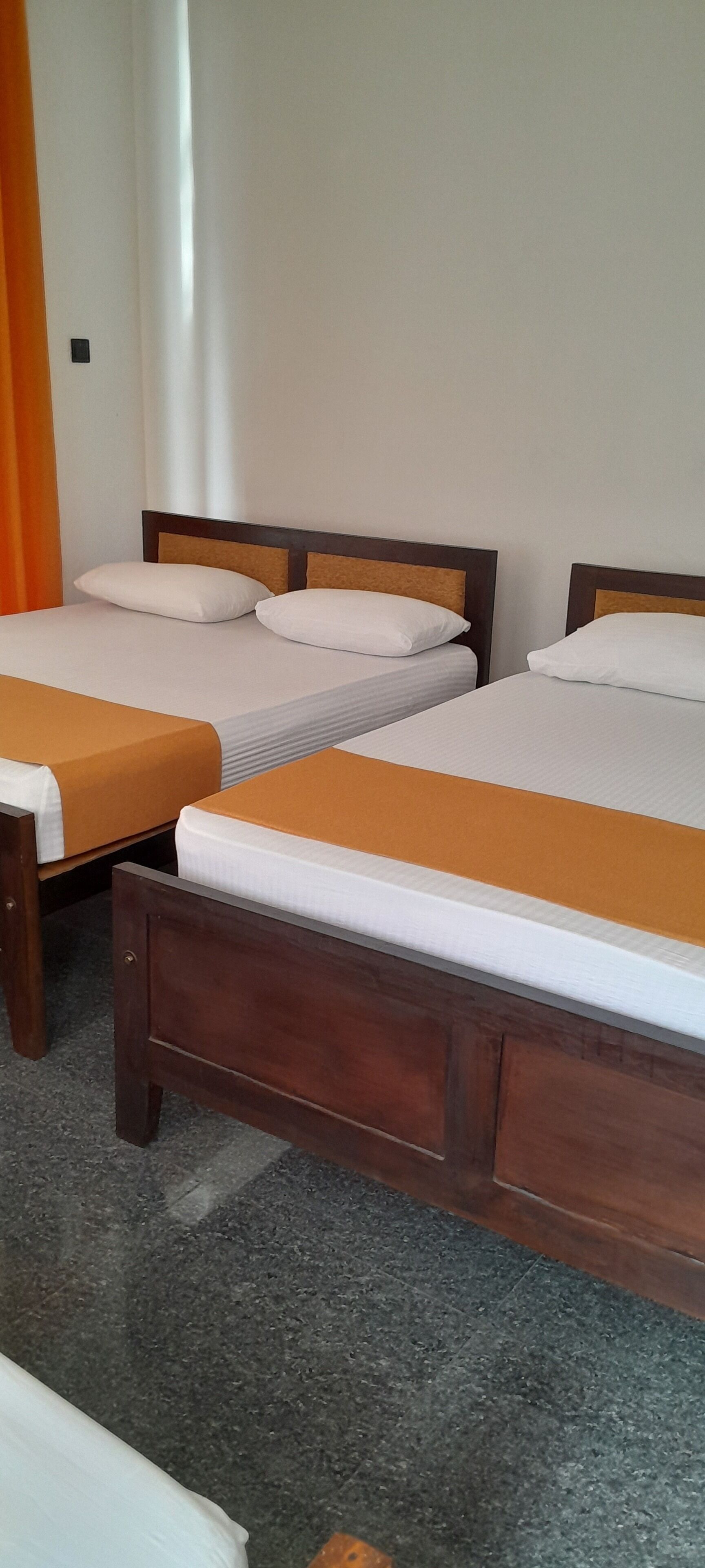 Une chambre d’hôtel avec trois lits en bois, chacun doté d’un matelas blanc et d’une couverture orange.