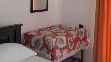 A bedroom with a bed, a bedside table, an air conditioning unit, a mirror, and a window with curtains.
