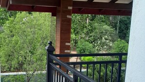 Een balkon met een zwart metalen hekwerk, een witte muur en uitzicht op een tuin met bomen en plantenpotten.