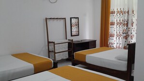 Een kamer met drie eenpersoonsbedden, een bureau, een stoel, een ventilator en een wandairconditioner.