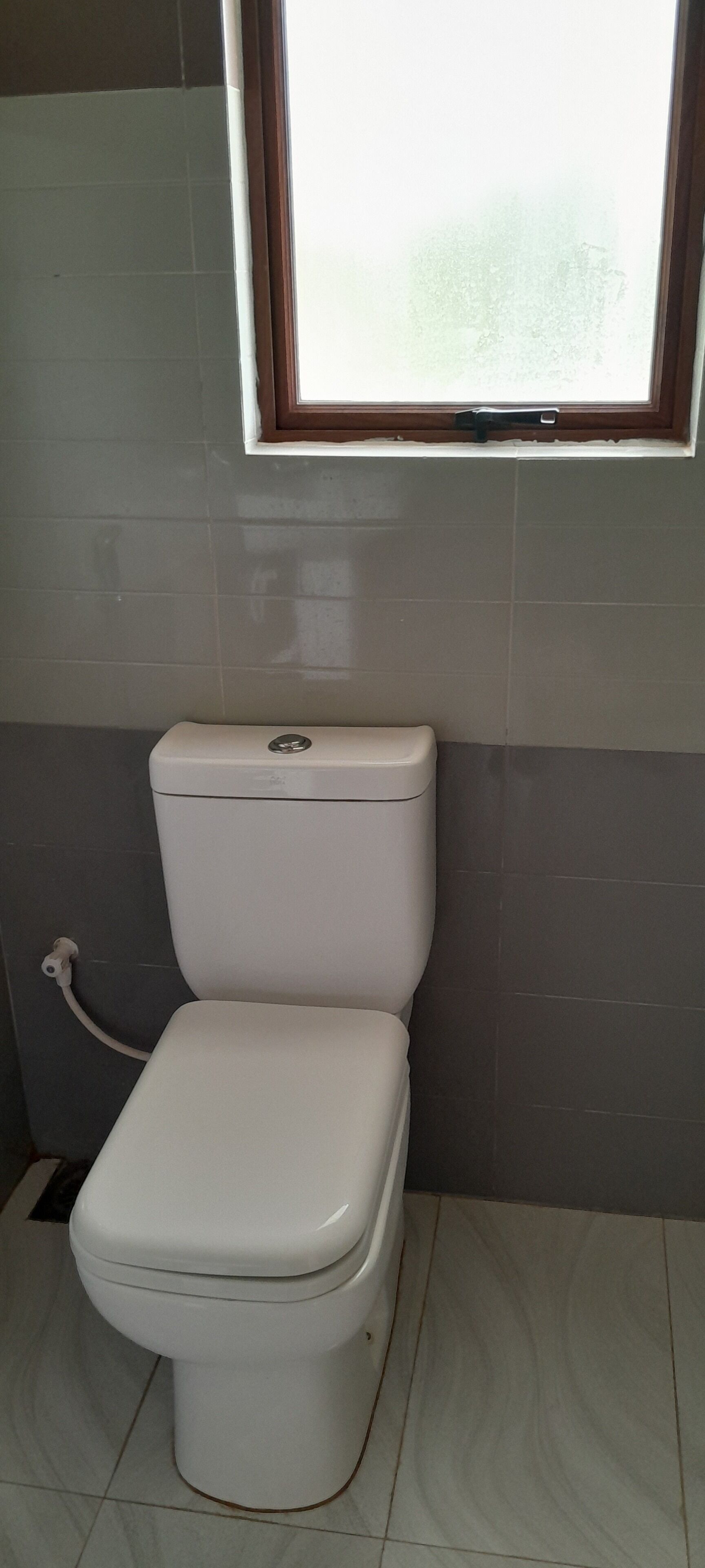A toilet in a bathroom with a window above it.