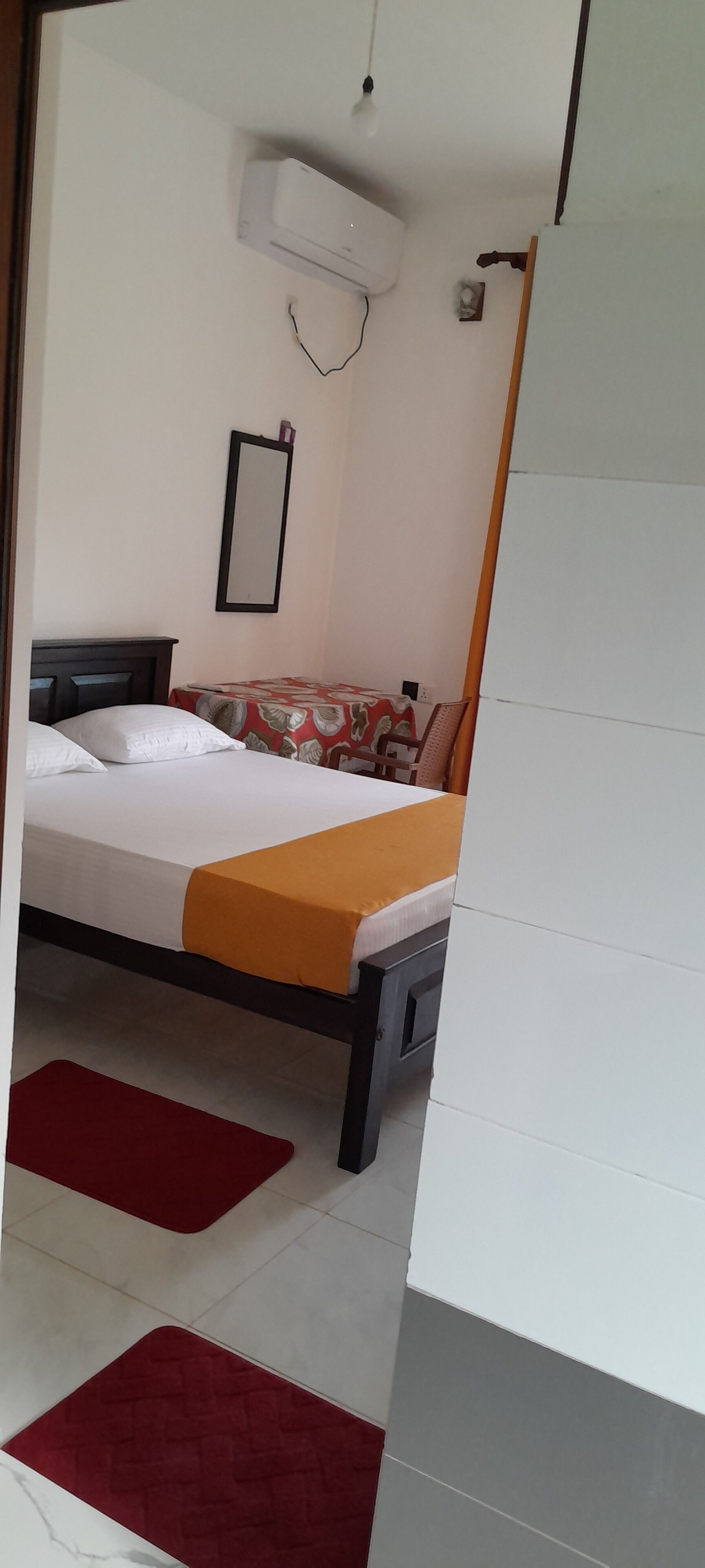 Een slaapkamer met een bed, nachtkastje, spiegel en een airconditioning.