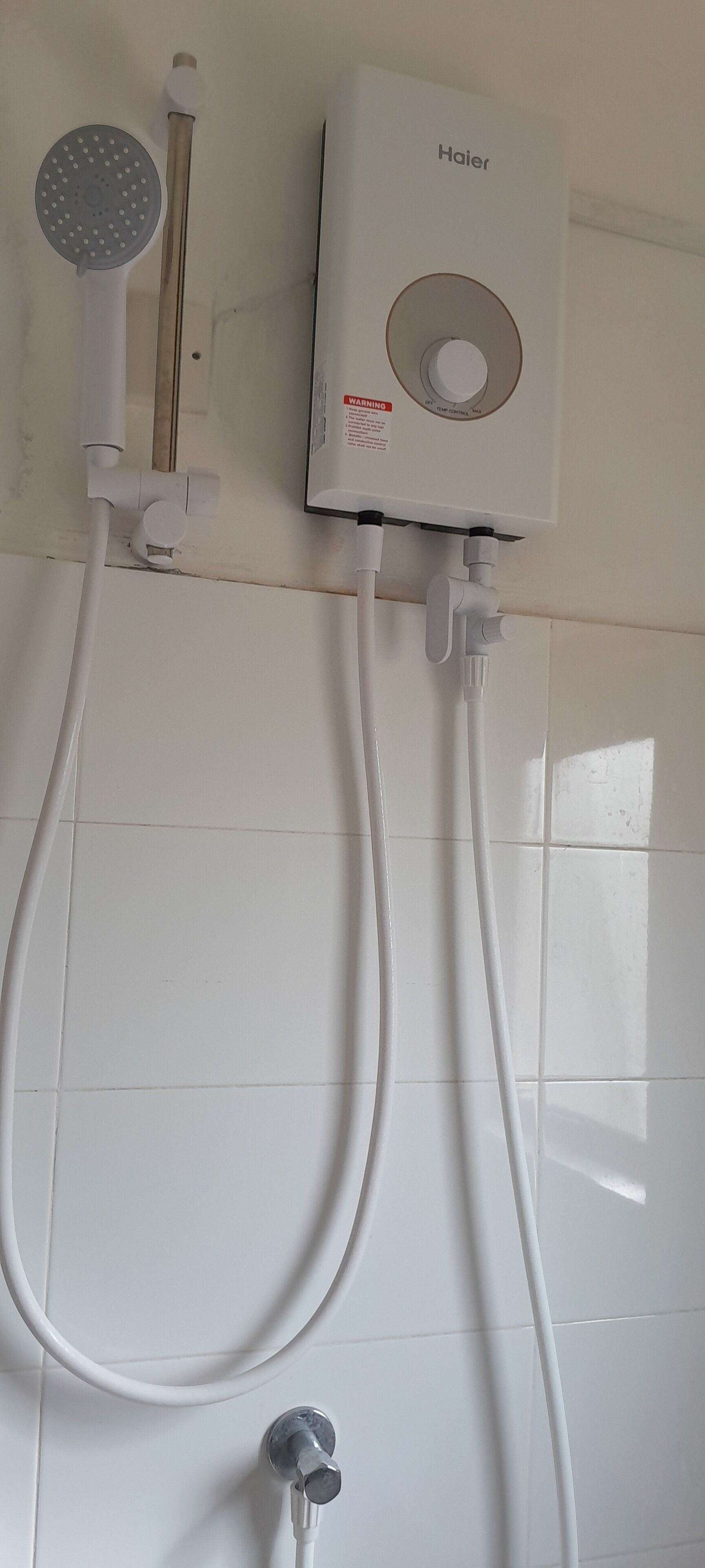 A bathroom with a white tiled wall, a Haier electric shower unit, and a handheld showerhead.