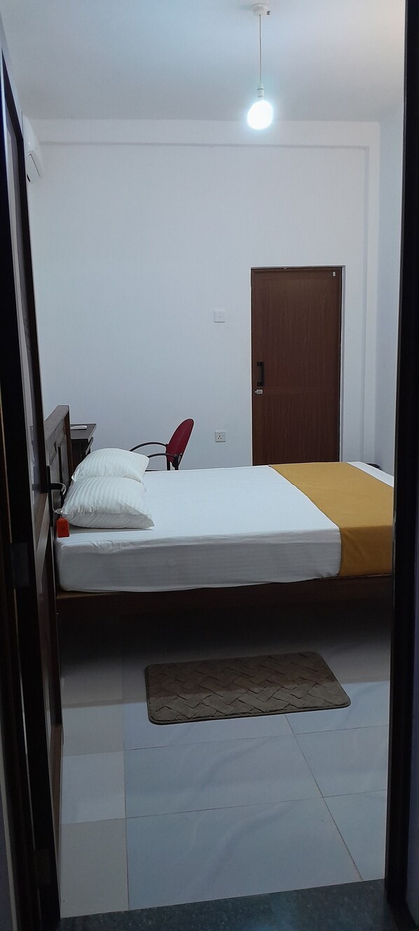 Une pièce avec un lit, une chaise rouge, une porte en bois et un luminaire au plafond.