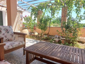 A patio with a wooden table and a floral sofa, surrounded by potted plants and a stone wall. - Chios Green Oasis (Chios)