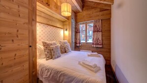 A wooden cabin bedroom with a bed, pillows, and a window with curtains. - Views of Bruson & Petit Combin range from the top floor of the Alpine residence (Val de Bagnes)