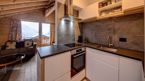 A modern kitchen with a built-in oven, a stainless steel range hood, and a wooden countertop. There is a window with a view of mountains and a sofa with a patterned throw. - Views of Bruson & Petit Combin range from the top floor of the Alpine residence (Val de Bagnes)