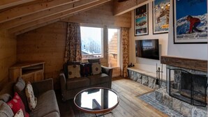 A cozy wooden cabin interior with a fireplace, a sofa, a TV, and a stone fireplace surround. - Views of Bruson & Petit Combin range from the top floor of the Alpine residence (Val de Bagnes)