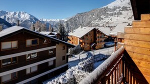 A wooden chalet-style building with a snow-covered roof, set against a backdrop of snow-capped mountains. - Views of Bruson & Petit Combin range from the top floor of the Alpine residence (Val de Bagnes)