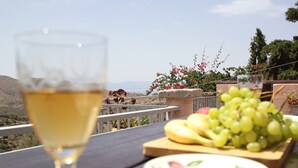 A table with a glass of white wine, a plate of fruit, and a bowl of green grapes. - Olive House by Frangki (Aegina)