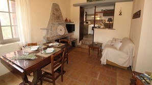 A dining area with a stone oven, a kitchen in the background, and a covered sofa. - Olive House by Frangki (Aegina)