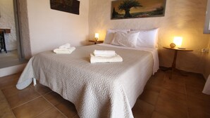 A neatly made bed with a textured blanket, two bedside lamps, and a painting of a tree on the wall. - Olive House by Frangki (Aegina)