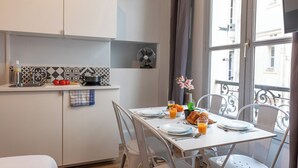 A modern kitchen with white cabinets, a patterned backsplash, and a dining area with a table set for breakfast. - WS Hôtel de Ville - Musée Pompidou (Paris)
