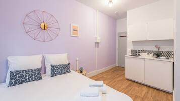 A modern bedroom with a large bed, geometric-patterned pillows, a wall clock, and a small bedside table.