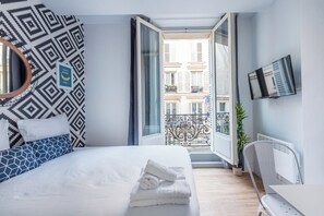 A hotel room with a bed, a TV, a balcony with a view of buildings, and a patterned wall. - WS Hôtel de Ville - Musée Pompidou (Paris)