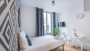 A modern hotel room with a bed, a desk, a chair, a TV, and a clock on the wall. - WS Hôtel de Ville - Musée Pompidou (Paris)