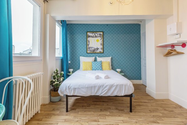 A bedroom with a bed, a potted plant, a radiator, and a window with curtains.
