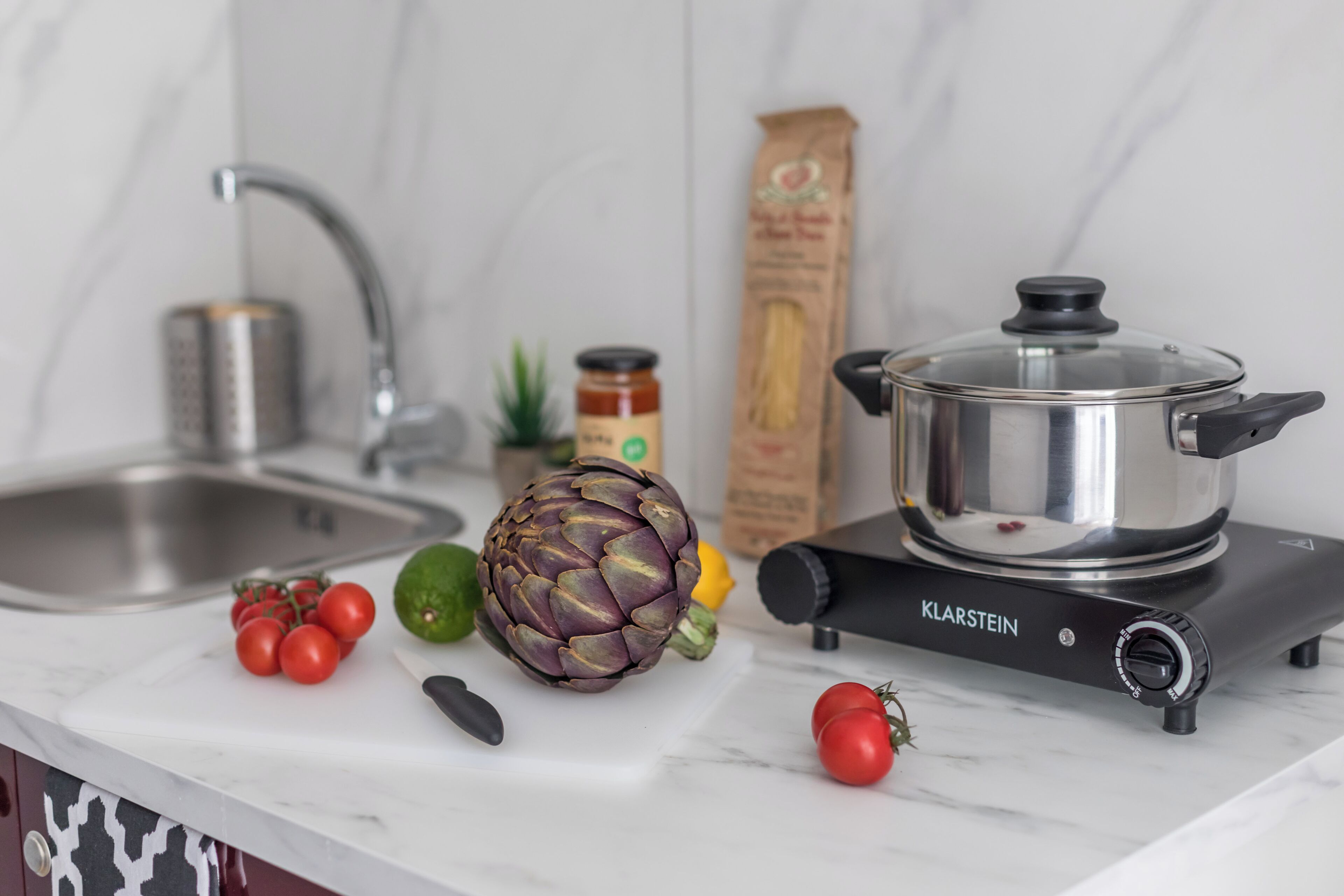 Una encimera de cocina con estufa, fregadero y diversos vegetales.