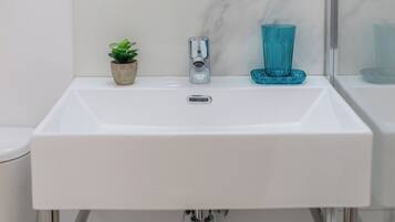 Ein weißes Waschbecken mit modernem Wasserhahn, eine kleine Topfpflanze und ein blaues Glas auf der Ablagefläche.