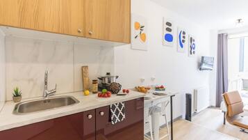 A modern kitchen with a marble countertop, wooden cabinets, and a built-in stove. There is a small plant on the counter and a window with curtains.