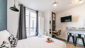A hotel room with a bed, a desk, a TV, and a breakfast bar. - WS Opéra - Rossini (Paris)