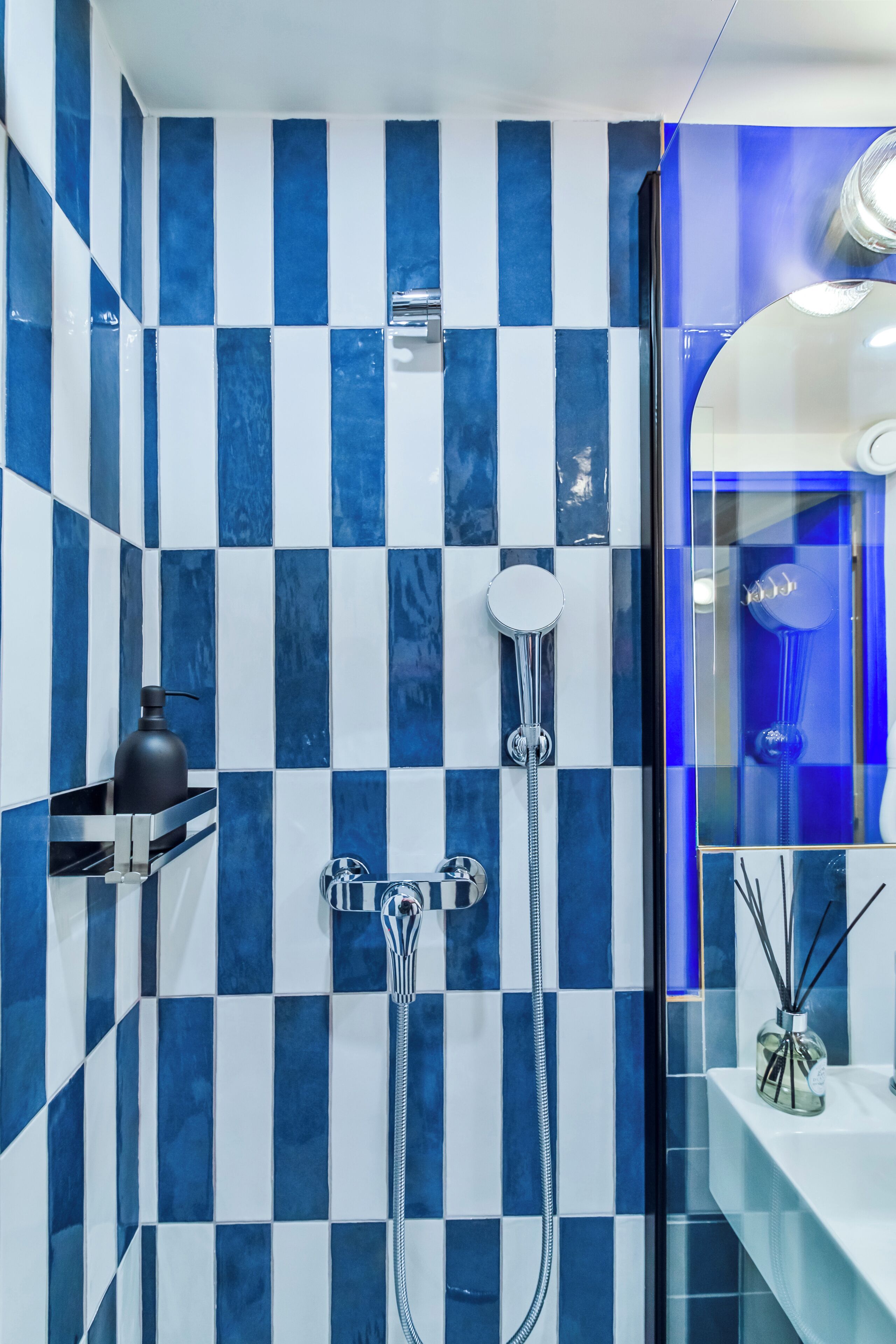 Une salle de bain avec un carrelage à motifs à carreaux, une douche, un miroir et une étagère sur laquelle se trouve une bouteille.