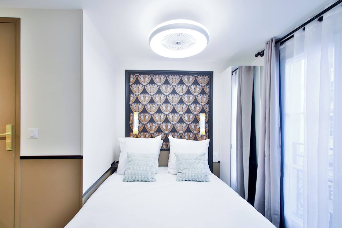 A hotel room with a bed, a patterned headboard, a window with curtains, and a door.