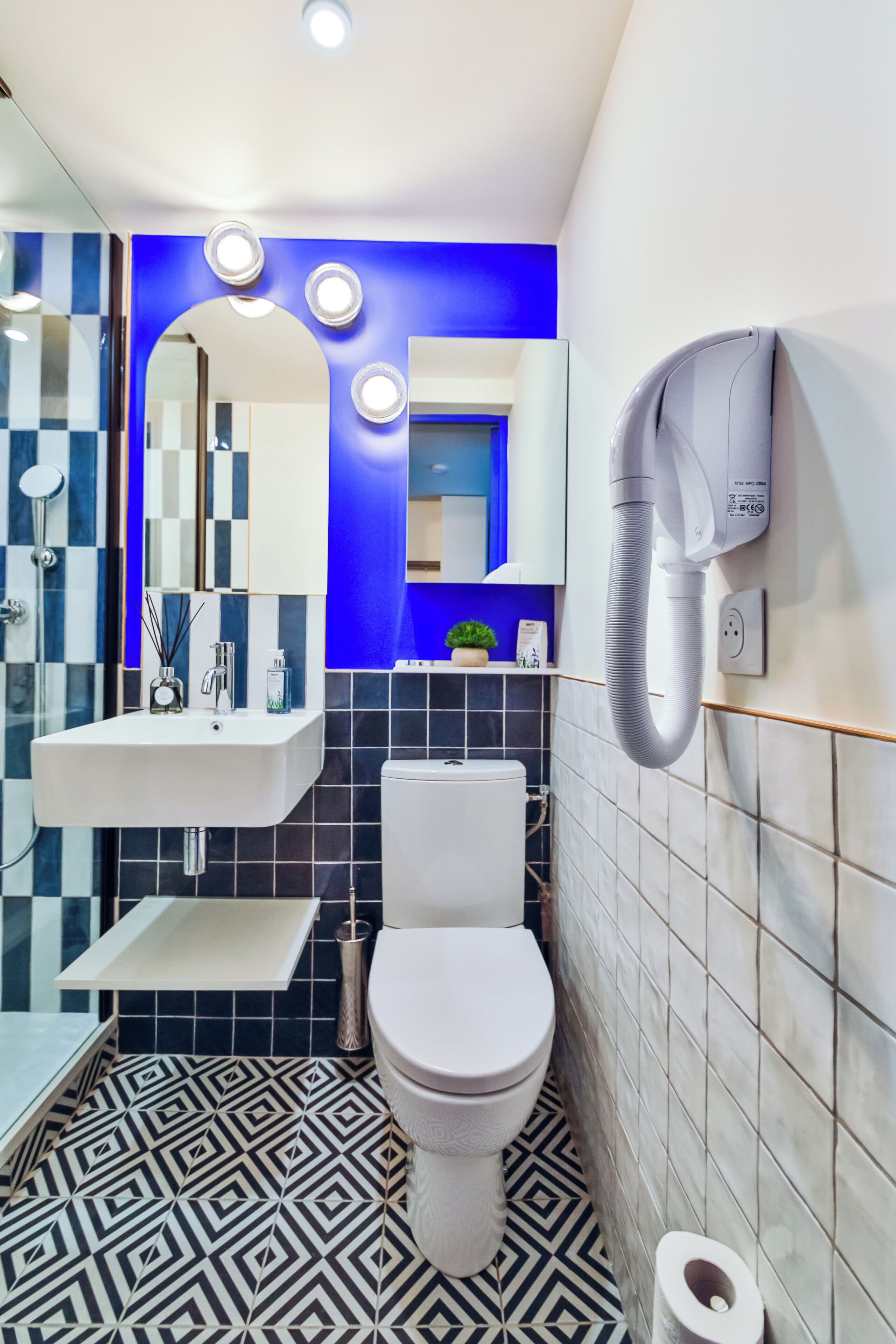 A modern bathroom with a white sink, a toilet, and a mirror. There is a hairdryer mounted on the wall.