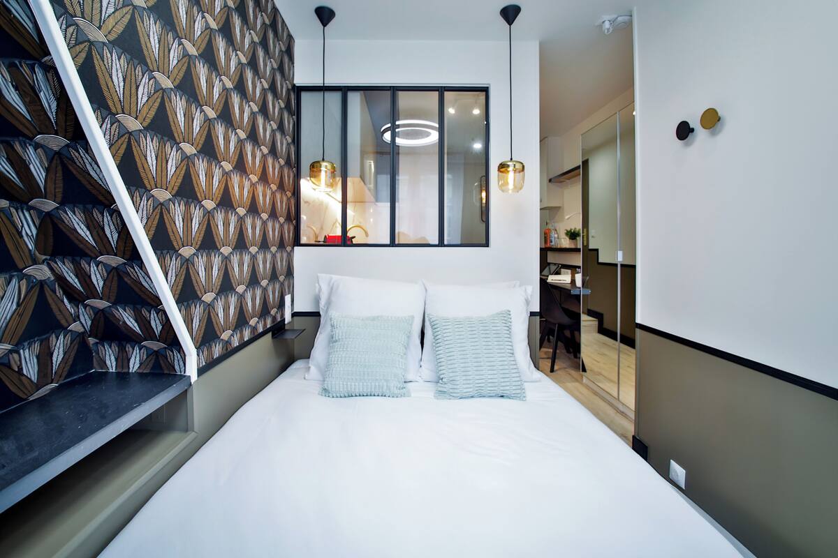 A modern bedroom with a large bed, two pillows, a nightstand, and a window with blinds.