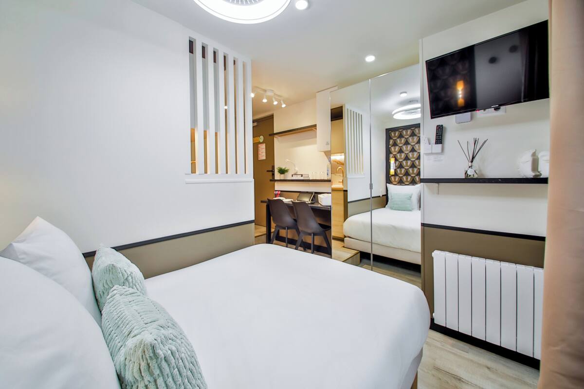 A modern hotel room with a large bed, a desk, and a TV mounted on the wall.
