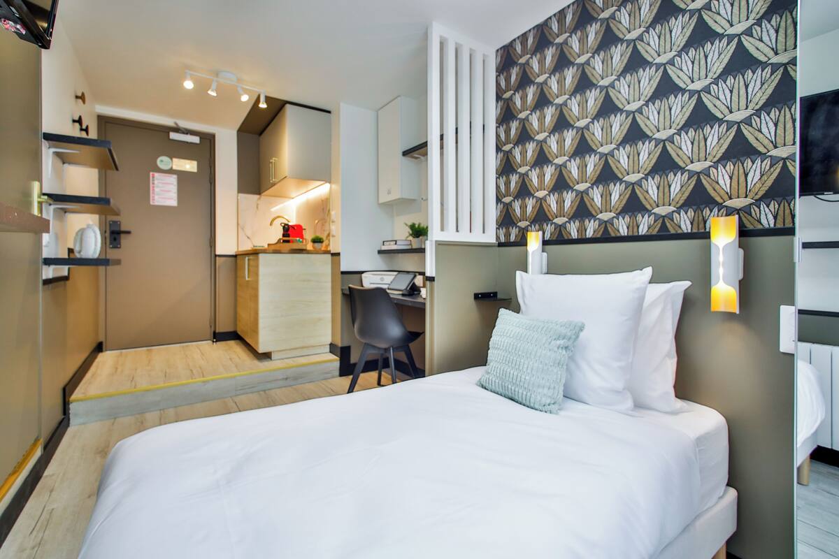 A hotel room with a bed, a desk, and a kitchenette.