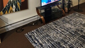 Un salon équipé d’un téléviseur à écran plat, d’une horloge, d’un ventilateur et d’un grand tableau abstrait accroché au mur.