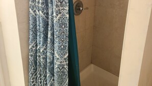 Une douche avec un rideau à motifs, une pomme de douche en métal et une étagère contenant des articles de toilette.