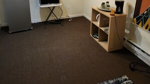 Une pièce compacte équipée d’un réfrigérateur, d’un four à micro-ondes, d’une machine à café et d’une petite table avec un grille-pain. Un tableau encadré est accroché au mur.