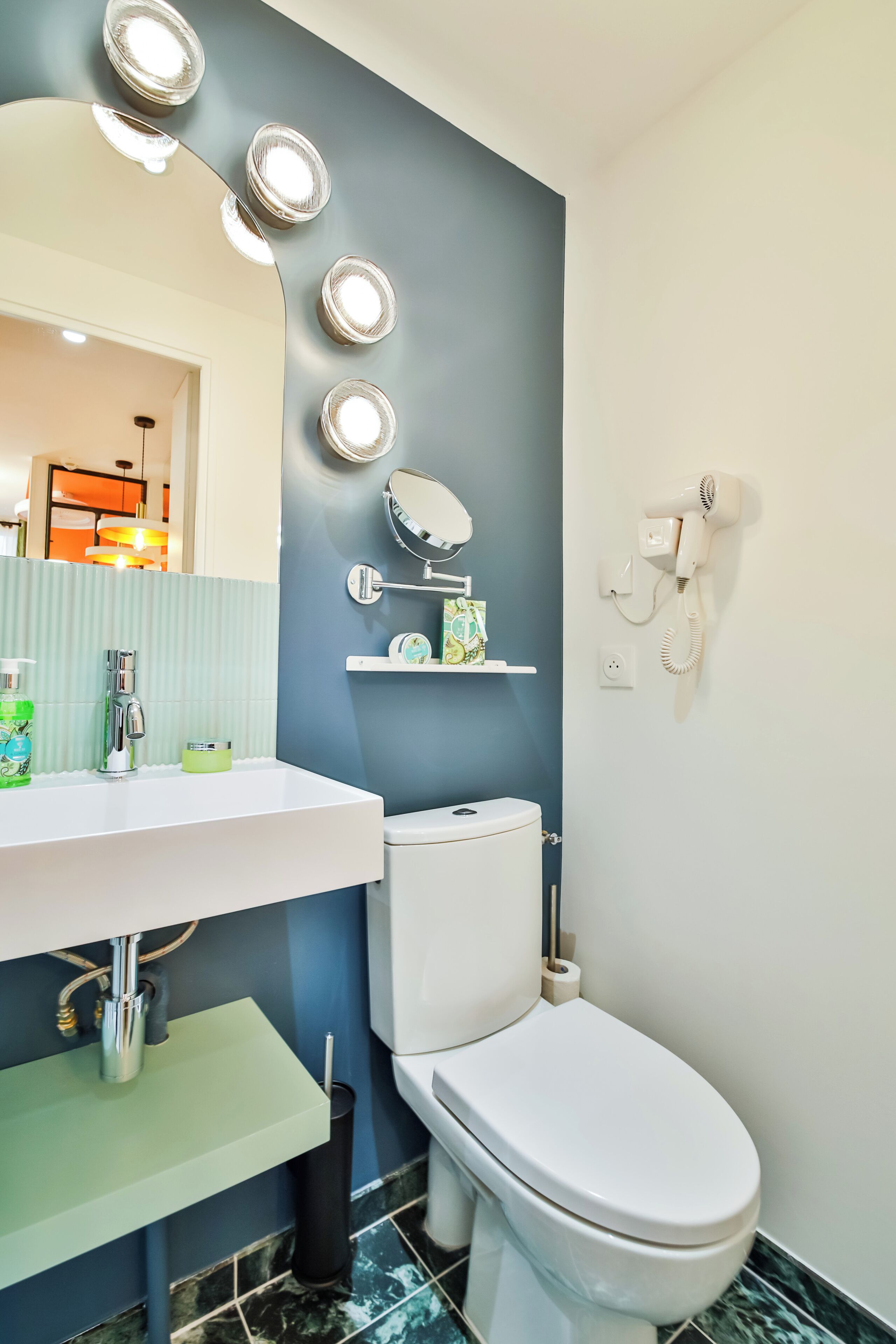 A bathroom with a white sink, a mirror, and a toilet. There are lights on the wall and a hairdryer mounted on the wall.