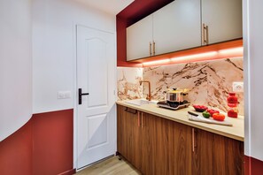 A compact kitchen with a white door, wooden cabinets, a marble backsplash, and a countertop with cooking utensils and fresh vegetables. - WS Opéra - Châteaudun (Paris)