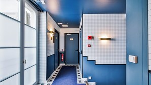 Un pasillo con alfombra azul, paredes de azulejos blancos y un extintor en la pared.