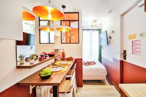 Cuina moderna amb taulell de fusta, llums pendents taronja i zona de menjador amb un llit al fons.