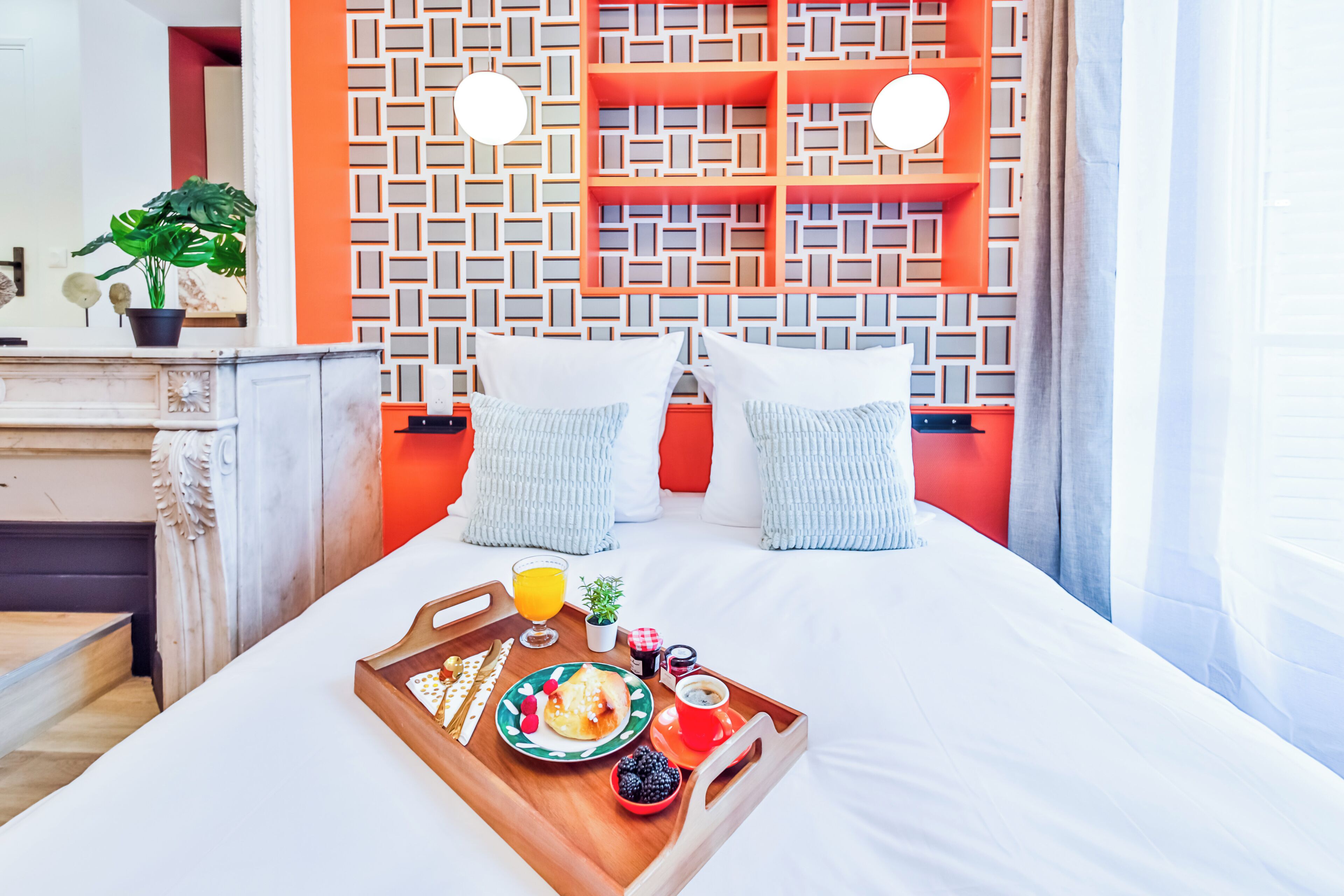 Een net opgemaakt bed met een dienblad ontbijtartikelen, een behang met patroon en een modern design.