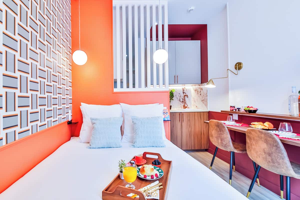 A modern hotel room with a bed, breakfast tray, and a dining area with chairs and a table.