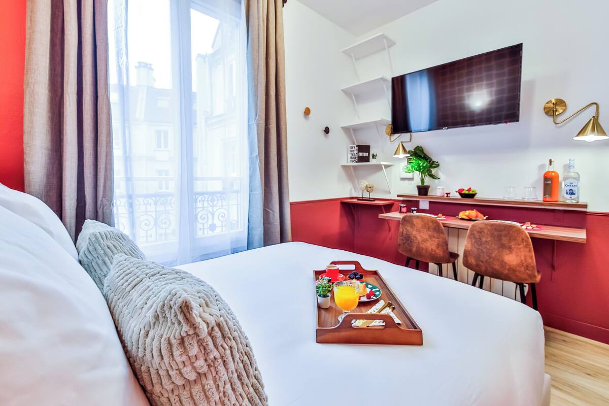 A hotel room with a bed, a breakfast tray, a TV, a desk, and a window with curtains.
