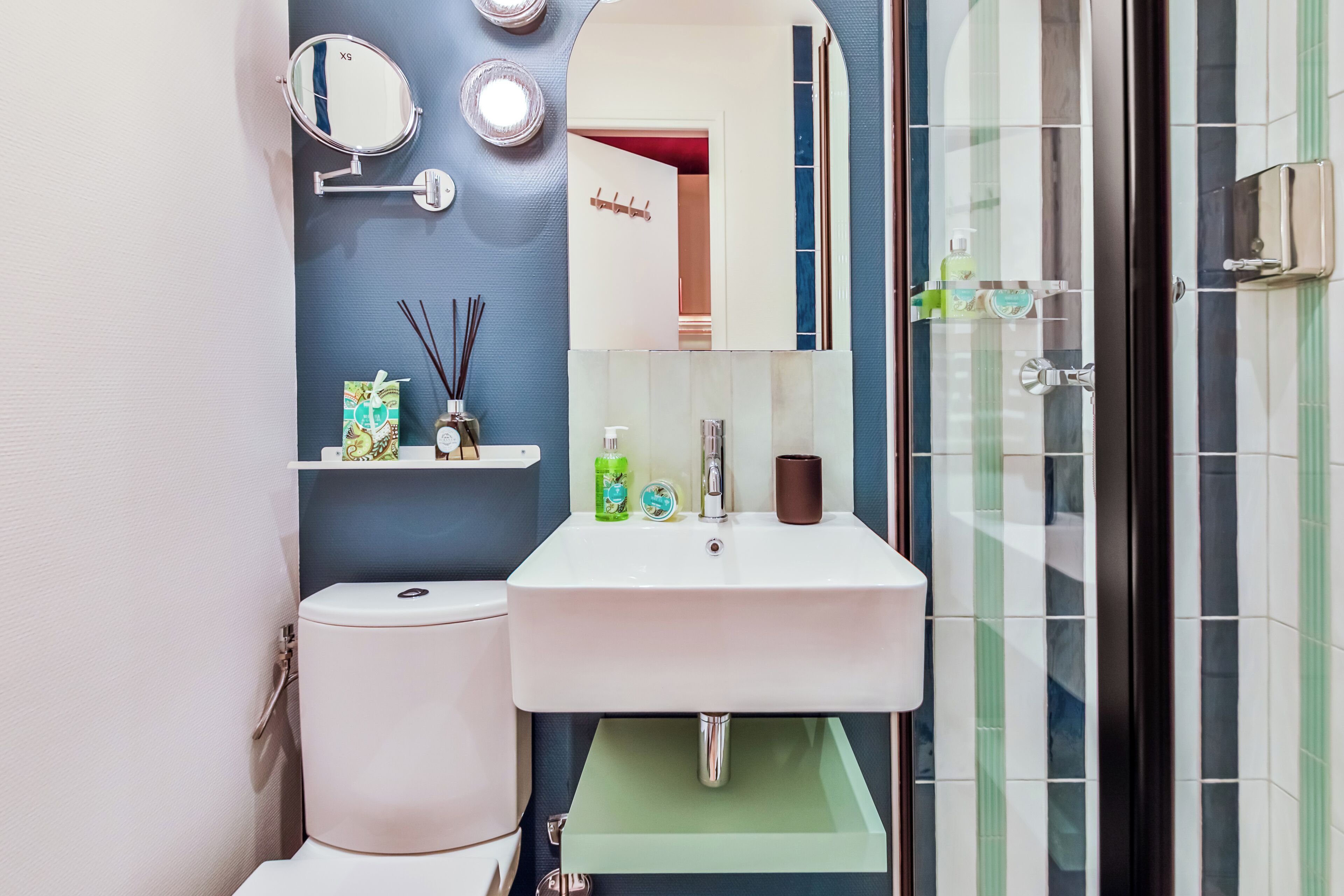 Une salle de bain avec un lavabo blanc, un miroir, des toilettes et un espace douche.
