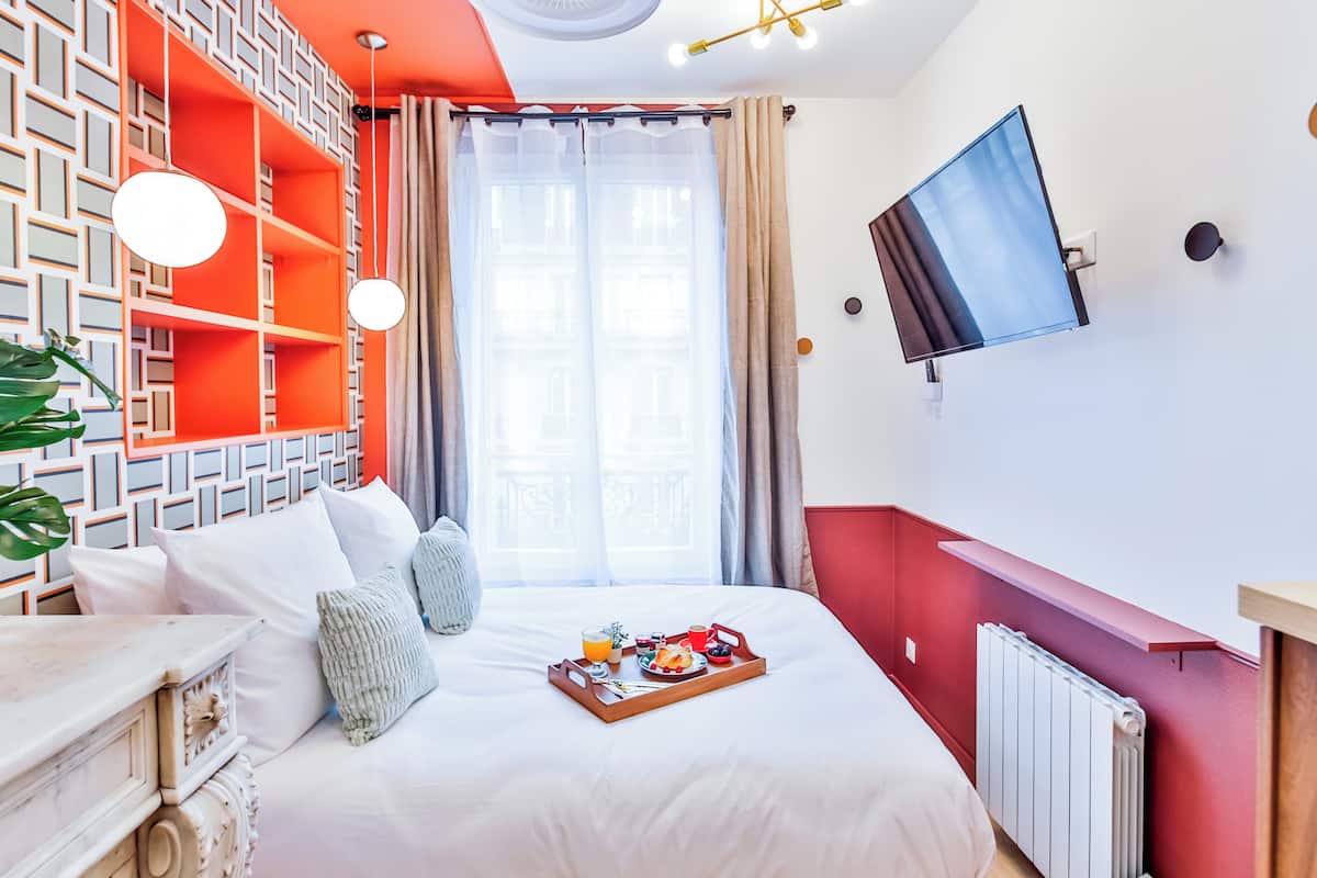 A hotel room with a bed, a breakfast tray, a TV, and a window with curtains.