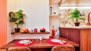 A dining area with a wooden table, two red placemats, a bottle of OREZZA, and a potted plant.