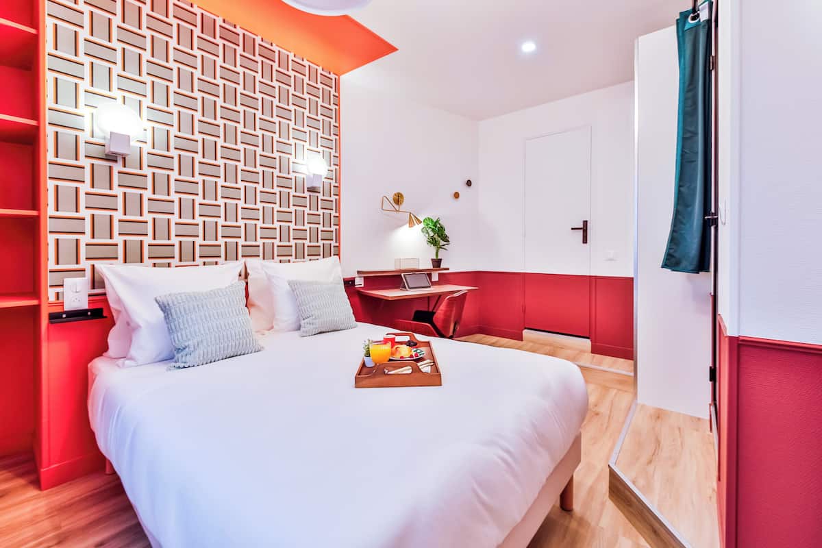 A hotel room with a large bed, a desk, and a red accent wall.