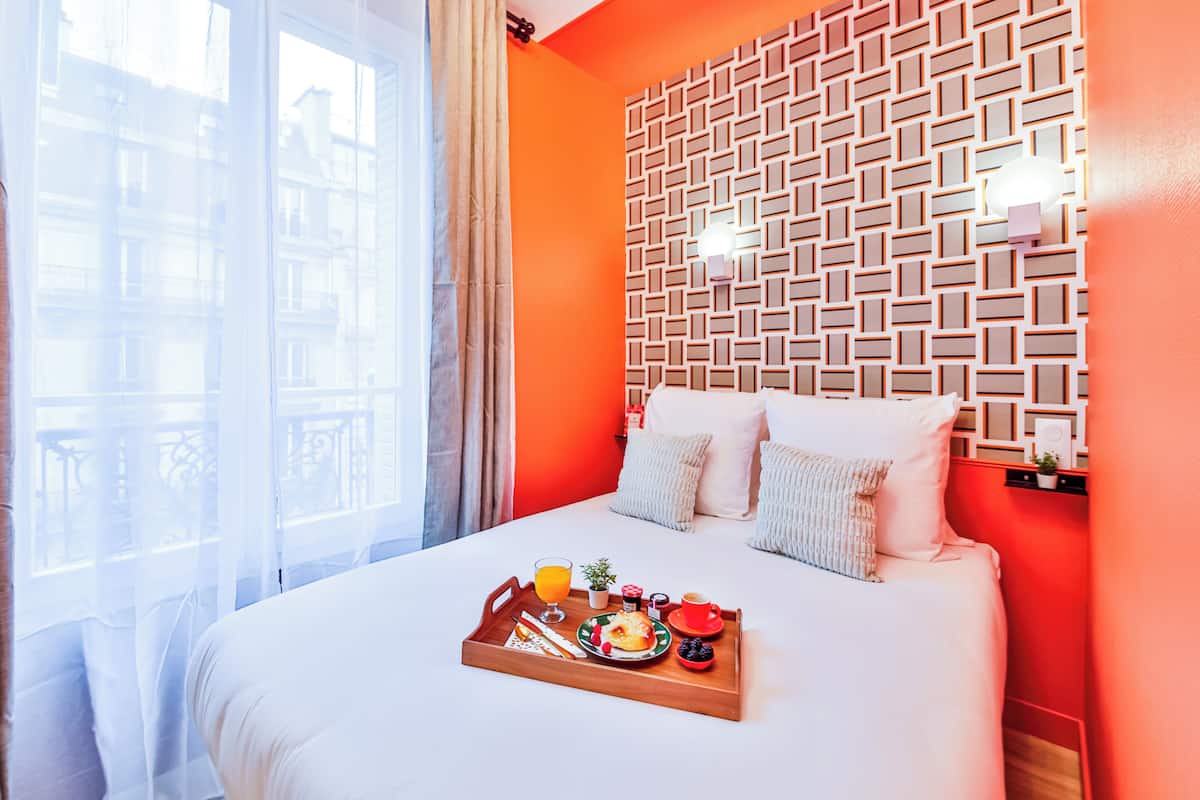 A hotel room with a bed, a breakfast tray, and a patterned wall.