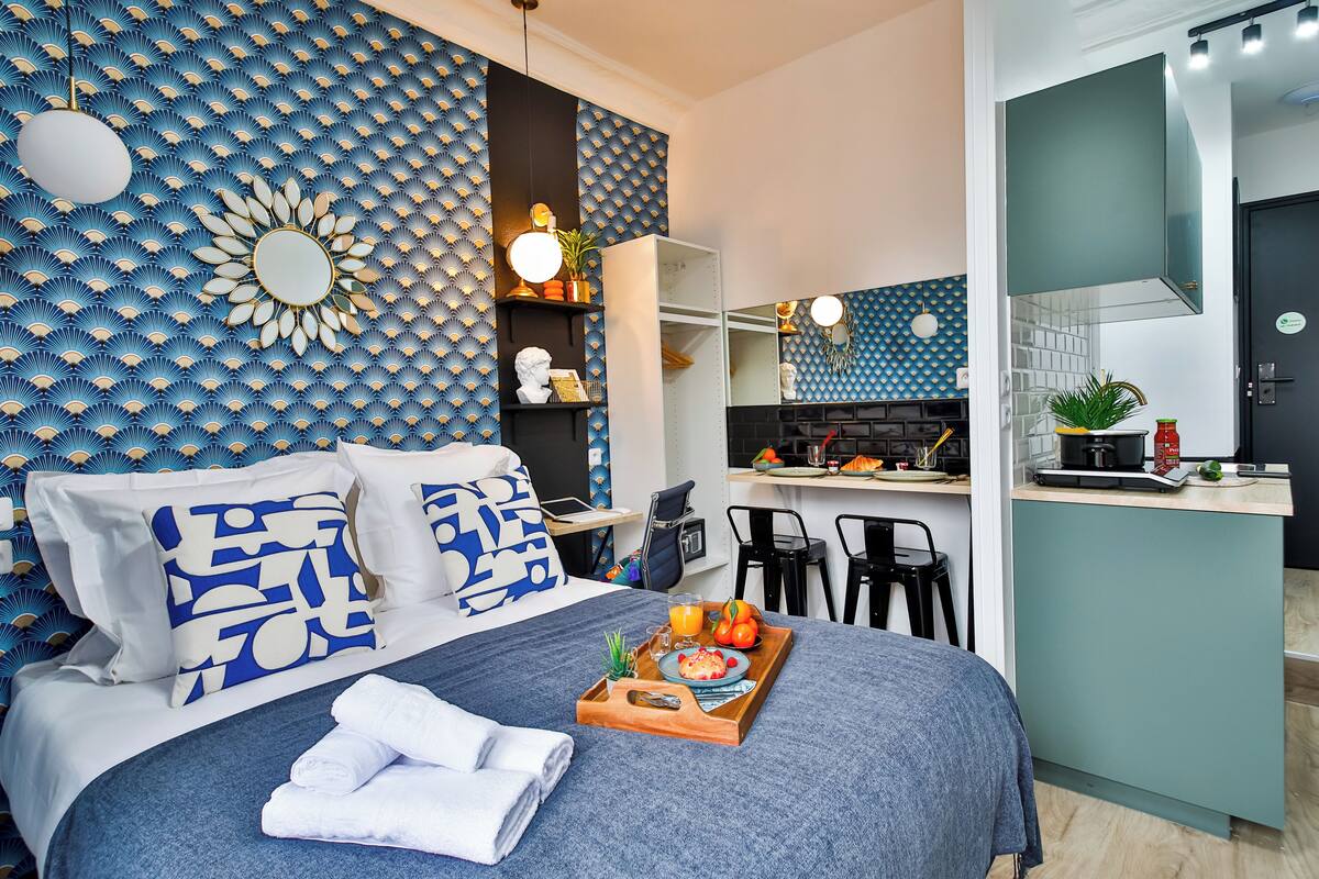 A modern hotel room with a bed, a breakfast tray, a kitchen area, and a bathroom.