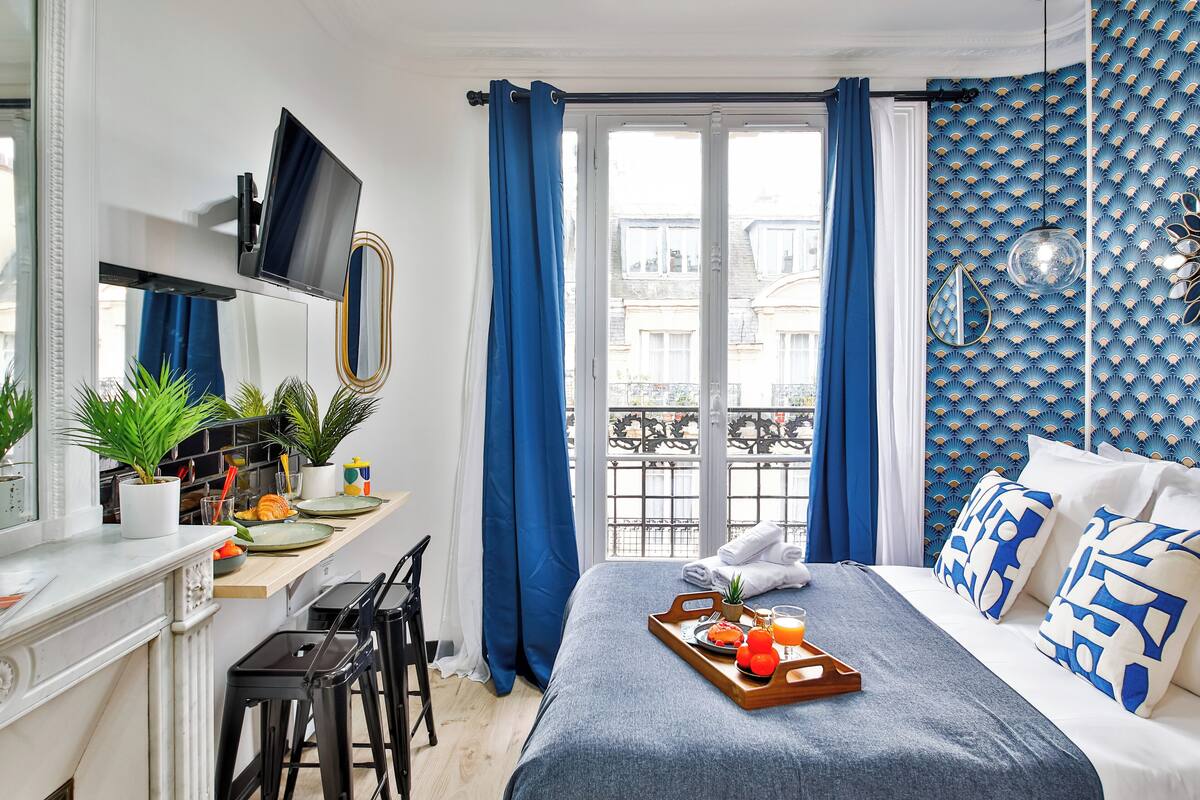 A modern hotel room with a bed, breakfast tray, potted plants, and a balcony view.