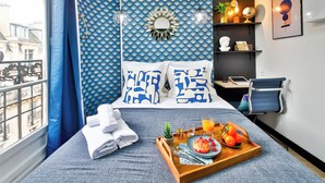 A hotel room with a bed, a tray with fruit and juice, a potted plant, and a view of buildings outside. - WS Tour Eiffel - Laos (Paris)