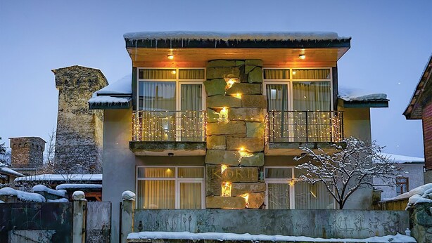 A multi-story building with stone facade, balconies with string lights, and snow on the roof and ground. - Korte Hotel Sleeps 14 With Courtyard (Mestia)